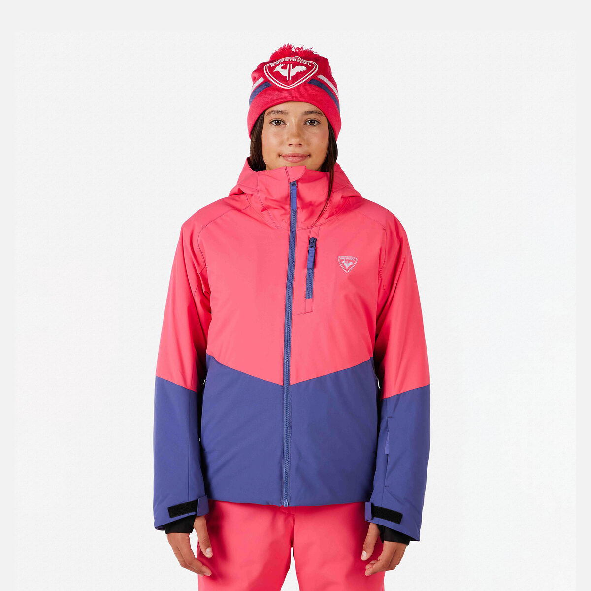 A girl wearing a pink and purple Rossignol Girls' Wispile Ski Jacket that is waterproof, insulated, breathable, and stretchable.