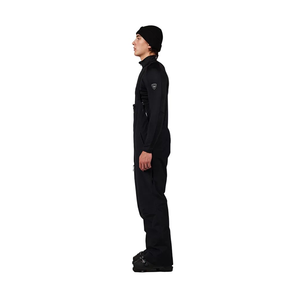 Side view of black Rossignol Men’s Outerlimits Insulated Bib Pants featuring high-chest bib construction, waterproof membrane fabric, adjustable shoulder suspenders, zippered thigh vents, integrated boot gaiters, and reinforced hem scuff guards.