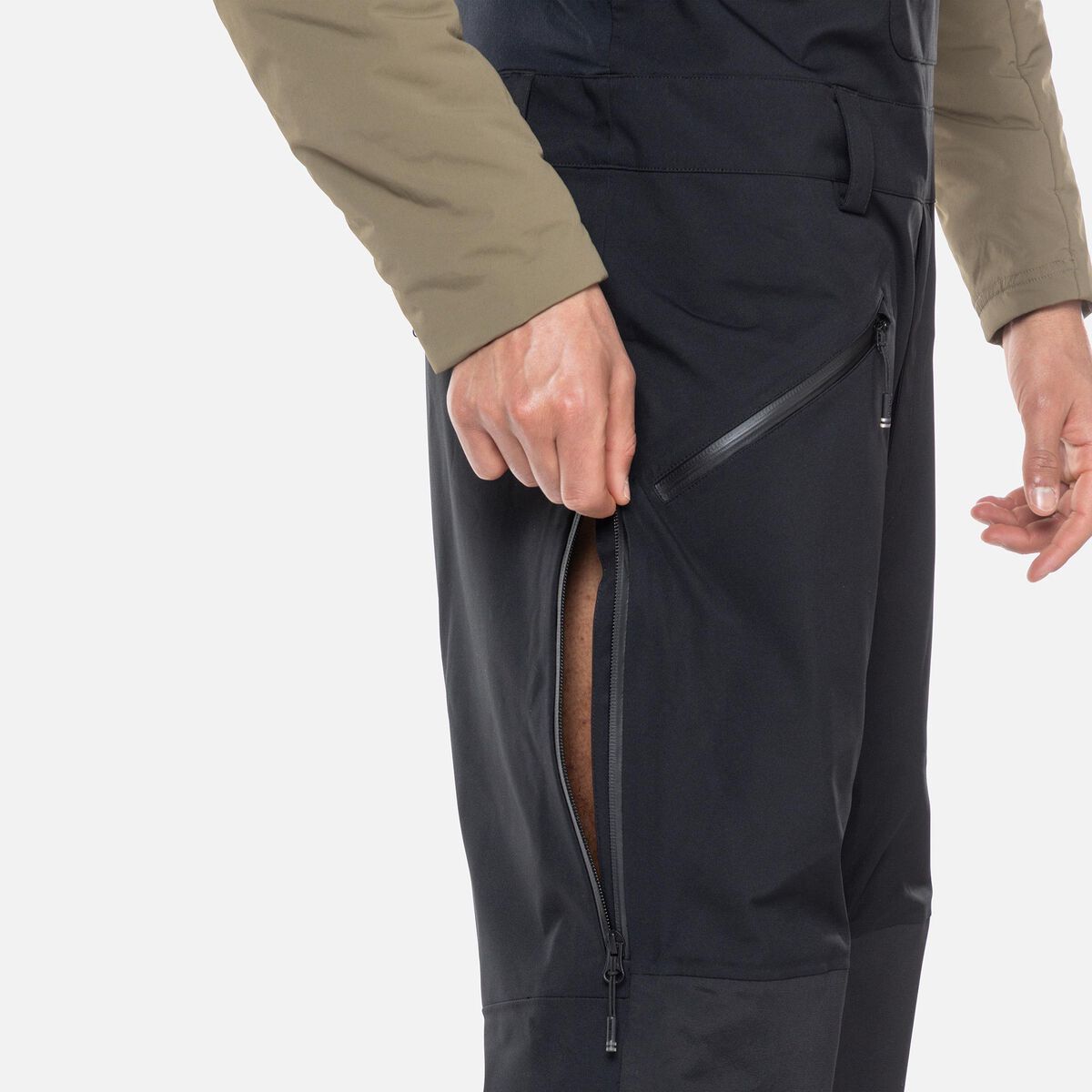 A close-up of a man wearing a pair of black Rossignol Men's SKPR 3L AYR Bib Pants that are waterproof, breathable, stretchable, warm, and include vents.