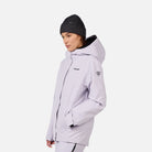 A woman wearing a light purple Rossignol Women's Desafio 2L Shell Ski Jacket that is lightweight, waterproof, breathable, and stretchable.