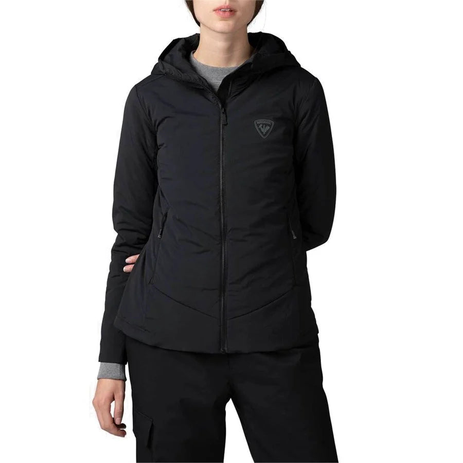 A woman wearing a black Rossignol Opside Hoodie Jacket with a hood, featuring a geometric logo on the chest and a visible brand tag on the sleeve.