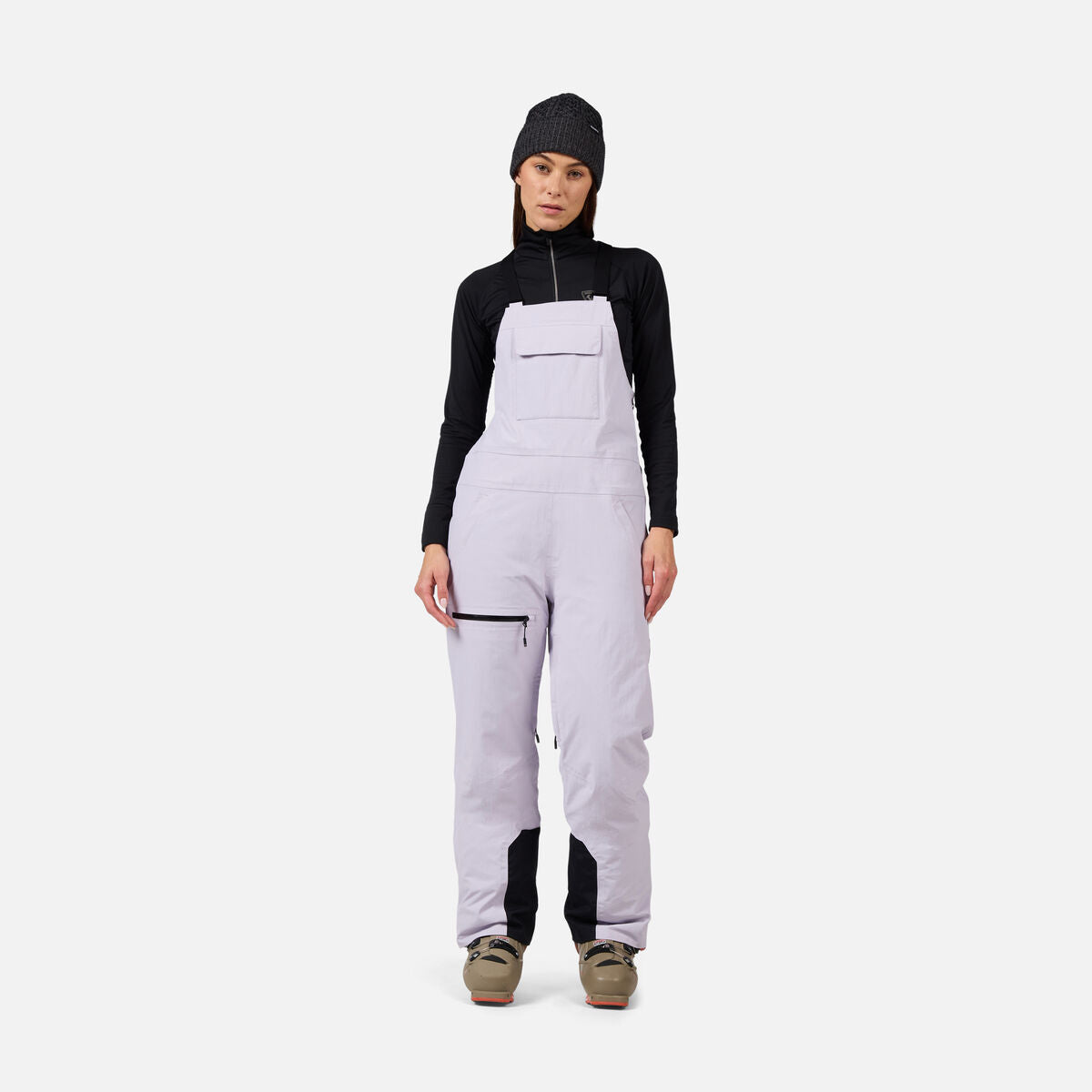 A woman wearing a pair of light purple Rossignol Women's Outer Limits Insulated Bib Ski Pants that are waterproof, breathable, stretchable, and warm.