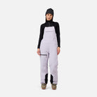 A woman wearing a pair of light purple Rossignol Women's Outer Limits Insulated Bib Ski Pants that are waterproof, breathable, stretchable, and warm.
