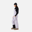 A woman wearing a pair of light purple Rossignol Women's Outer Limits Insulated Bib Ski Pants that are waterproof, breathable, stretchable, and warm.