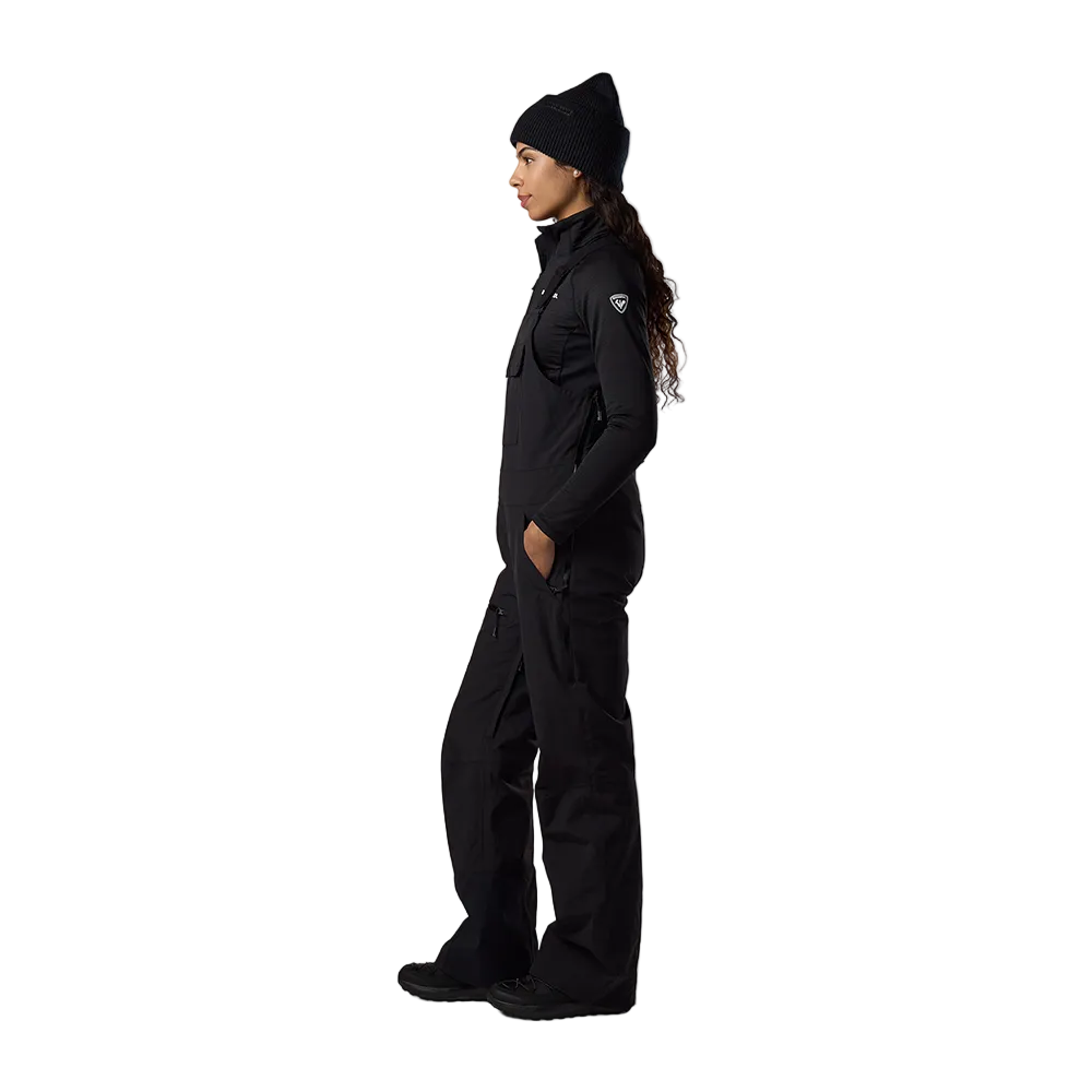 Side view of black Rossignol Women’s Outerlimits Insulated Bib Pants featuring high-chest bib construction, waterproof membrane fabric, adjustable suspenders, zippered inner thigh vents, integrated boot gaiters, and reinforced hem scuff guards.