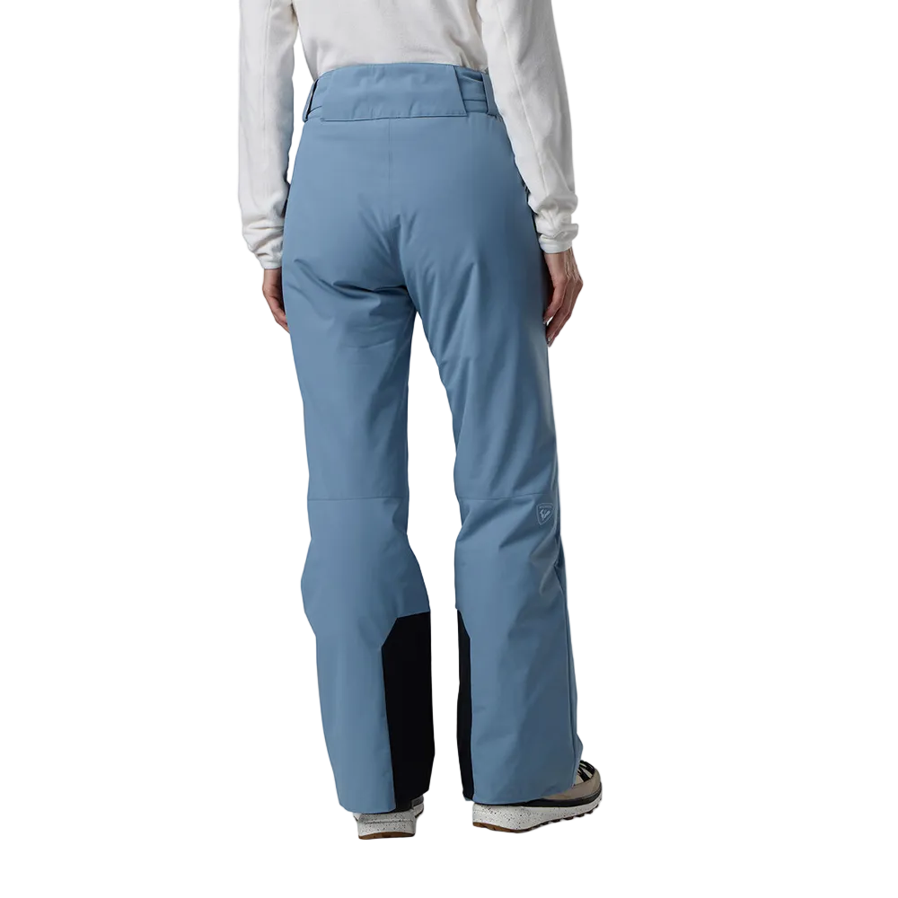 Rear view of the blue aura Rossignol Women’s Strawpile Insulated Pants featuring waterproof membrane fabric, recycled synthetic insulation, adjustable waist tabs, integrated boot gaiters, and reinforced hem scuff guards.
