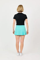 Woman wearing a black top and teal Sofibella UV Staples 14" Panel Skort on a white background