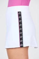 Woman wearing white Sofibella Women's Pinkology 14" Skort with black and white star detailing on a white background