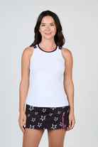 Woman wearing a white Sofibella Women's Pinkology Baseline Tank Top and black shorts with star pattern on a white background