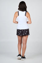 Woman wearing a white Sofibella Women's Pinkology Baseline Tank Top and black shorts with star pattern on a white background