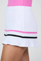 Woman wearing a pink tank top and white Sofibella Women's Style Icon 14" Skort with black and pink stripes on a white background