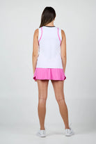 Woman wearing a white Sofibella Womens Style Icon Full Back Tank Top with pink trim and a matching pink skirt on a light gray background