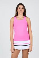 Woman wearing a pink Sofibella Women's Style Icon Racerback Tank Top and white skirt with black trim on a light gray background