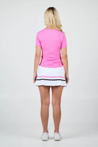 Woman wearing a pink Sofibella Women's Style Icon T-Shirt and white skirt with a black trim on a light gray background
