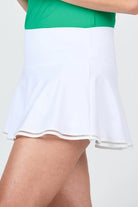 A woman wearing a green rank top and a white Sofibella Women's UV Staples 13" Skort on a white background