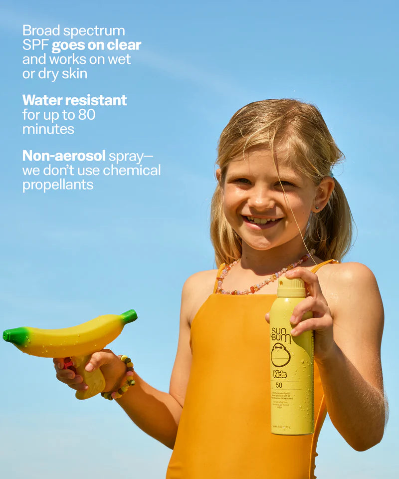 A child holding a yellow Sun Bum Kids SPF 50 Clear Sunscreen spray bottle on a blue background