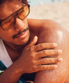 A man on a beach applying Sun Bum Original SPF 30 Sunscreen Lotion to his shoulder