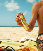 A man holding a Sun Bum SPF 45 Face Mist bottle on a beach
