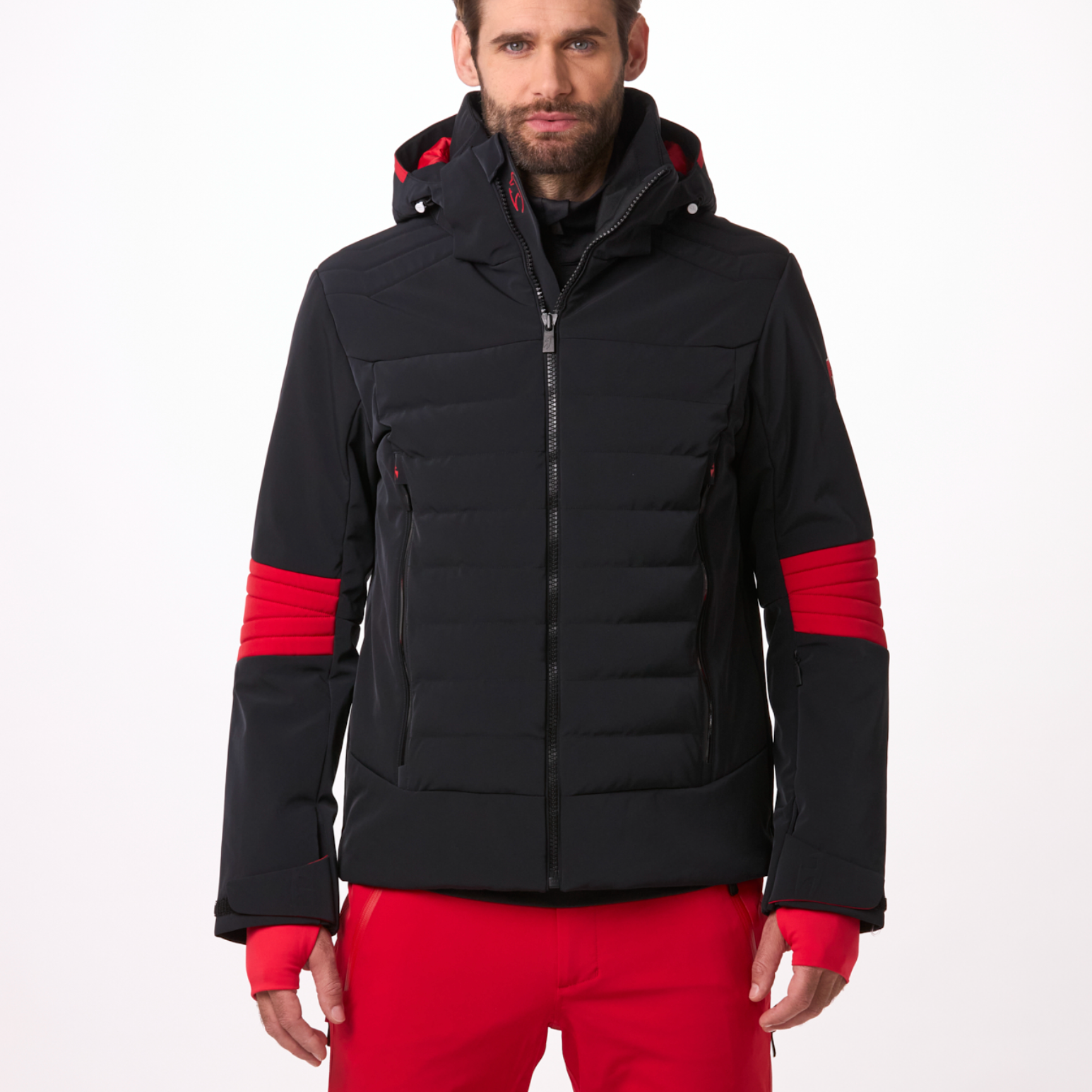 A man wearing a black and red Toni Sailer Men's Matti Ski Jacket made from premium fabrics and insulation that is waterproof, breathable, stretchable, insulated, and fashionable.