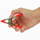 A hand holding a Wintersteiger Greatneck 1" Steel Spring Clamp showing nickel-plated steel body, high-tension coil spring, 1-inch jaw opening, non-marring vinyl-dipped jaw tips, and red vinyl-coated handles.